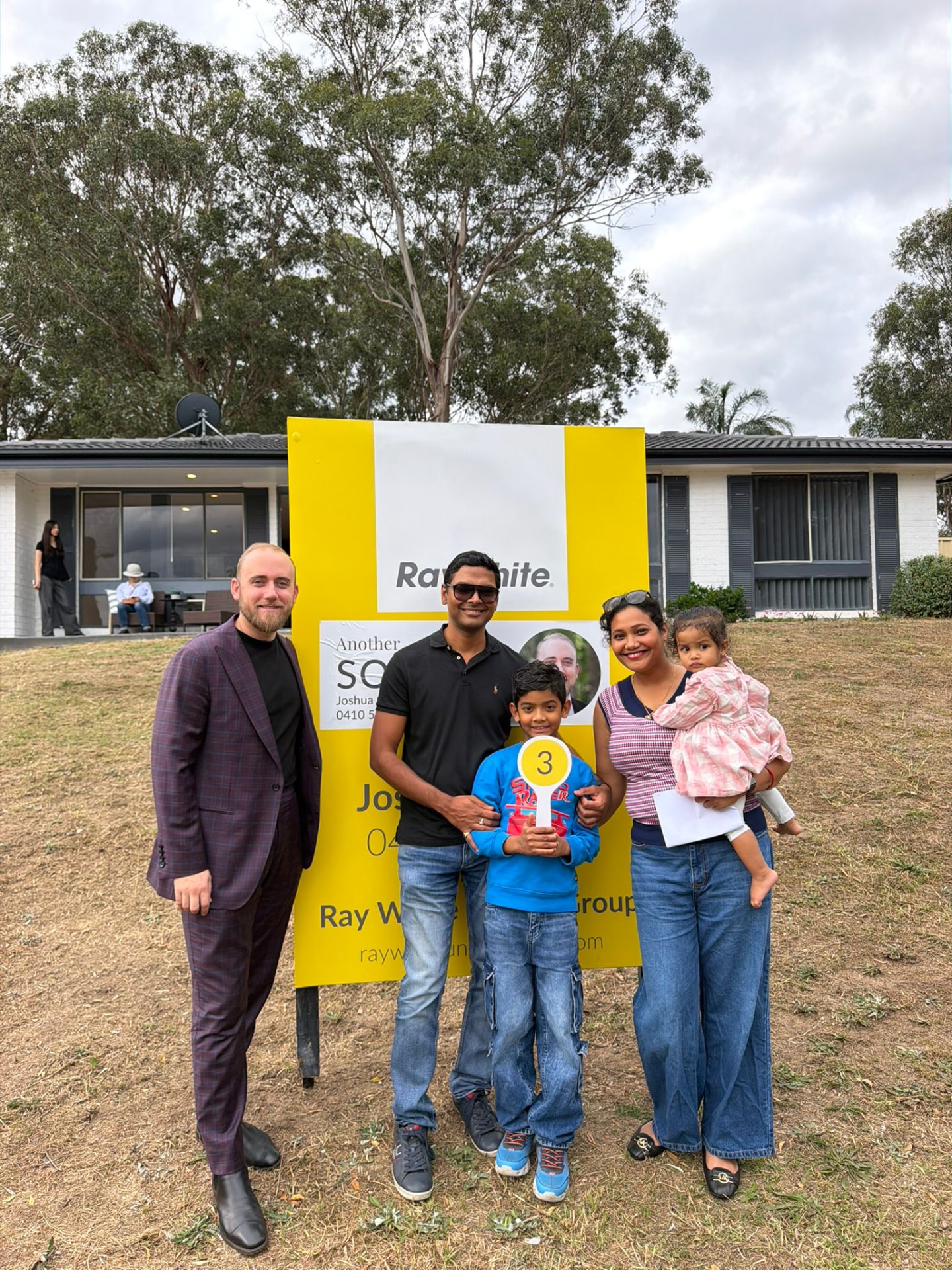 A family of four beside a Sold sign at their home